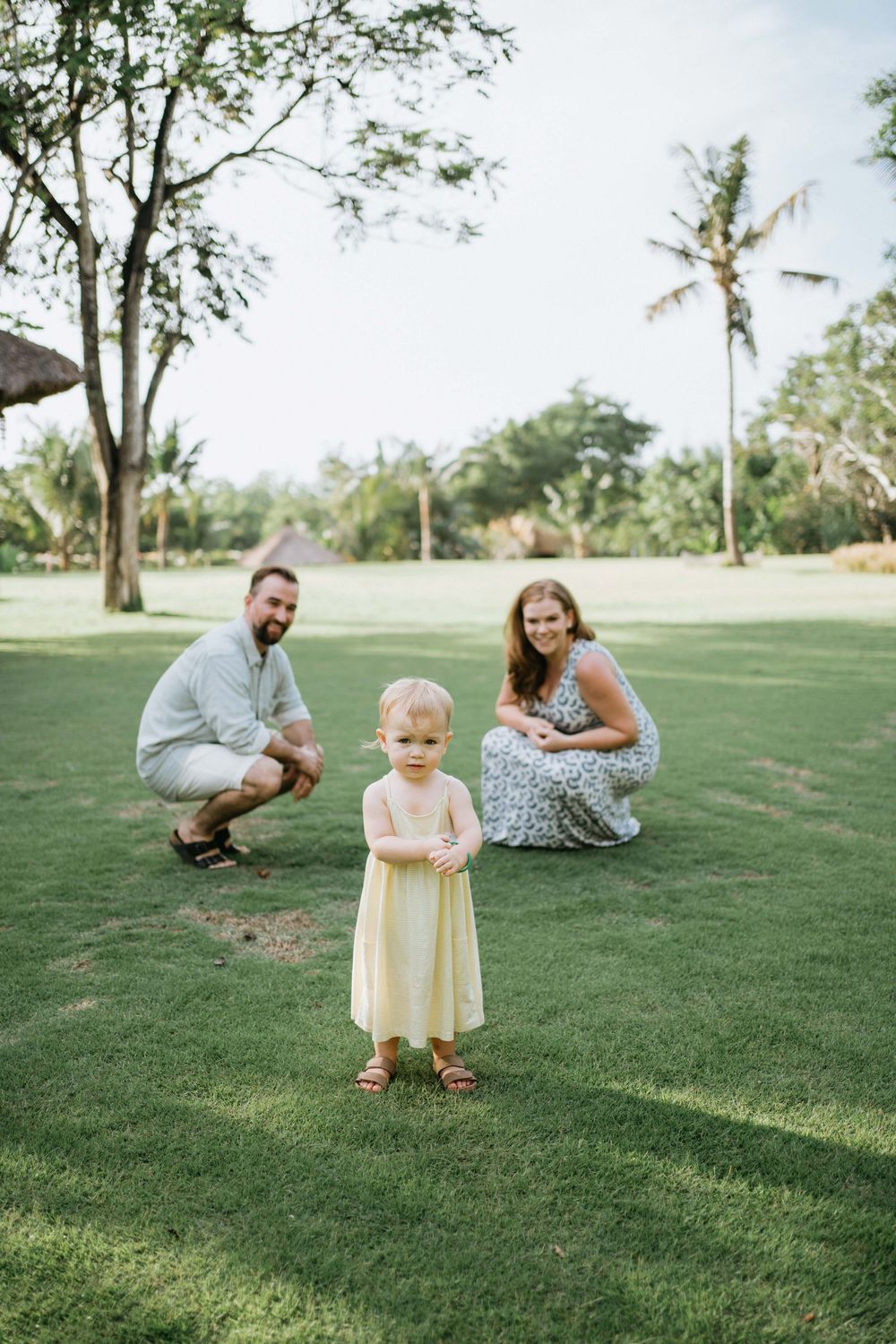 A family spending time together on a sunny grassy lawn with palm trees in the background.