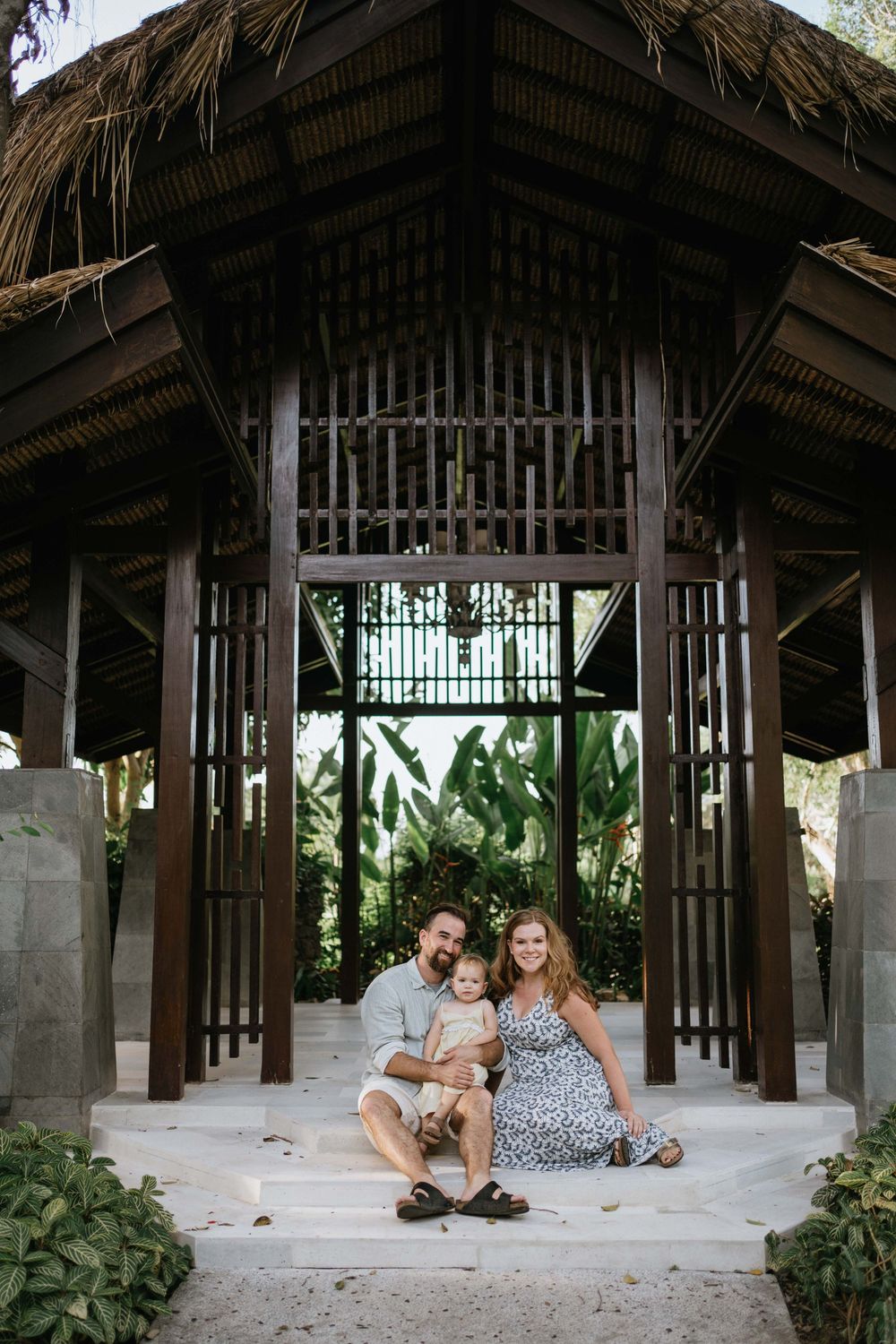 Family relaxing under a rustic thatched-roof pavilion in a tropical setting.