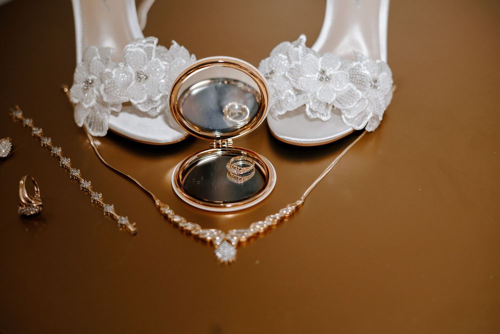 Bridal accessories flat lay with white heels, pearl necklace, earrings, and gold compact mirror.
