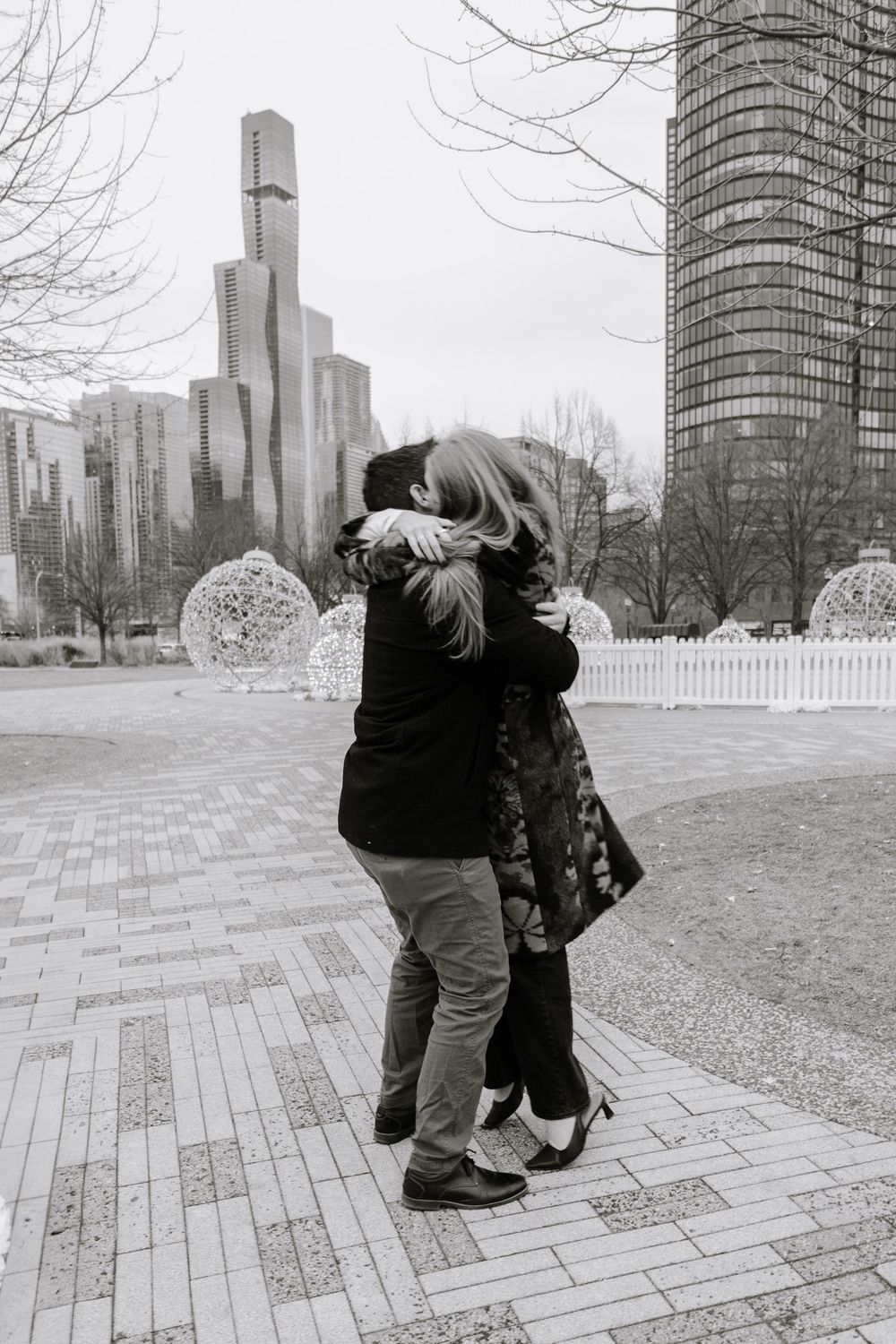 A sequence of four black and white photos showing a couple embracing against a city skyline backdrop in a park setting.