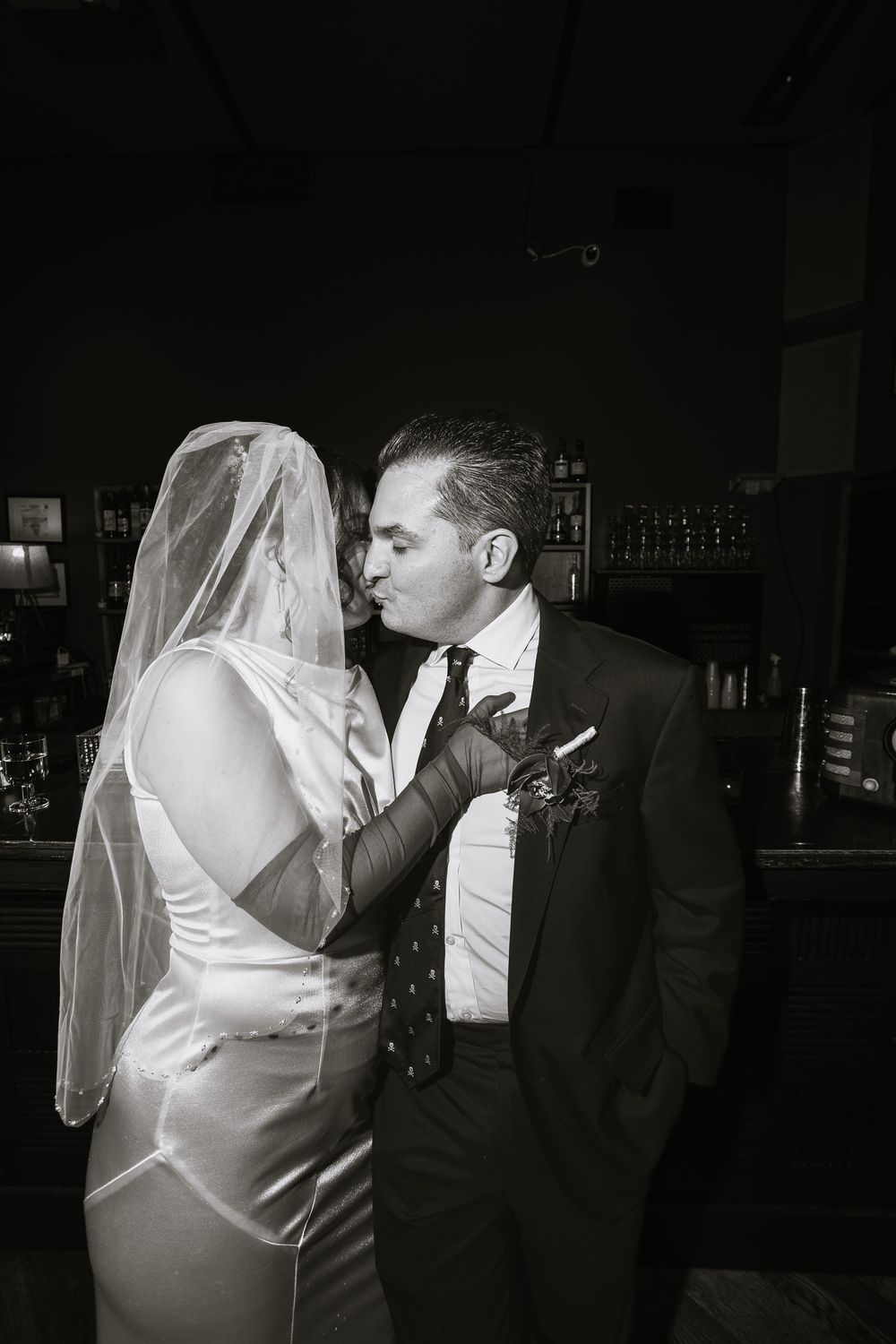 Black and white romantic photo of bride and groom sharing a kiss at their wedding reception bar.
