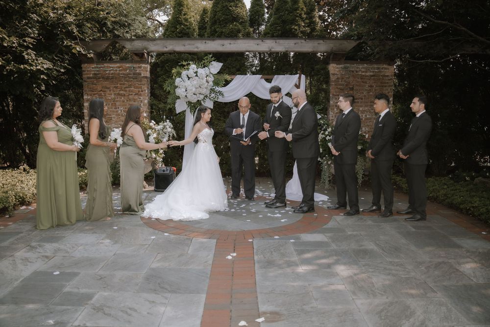 Wedding party members stand in formation on a stone patio during an outdoor ceremony.