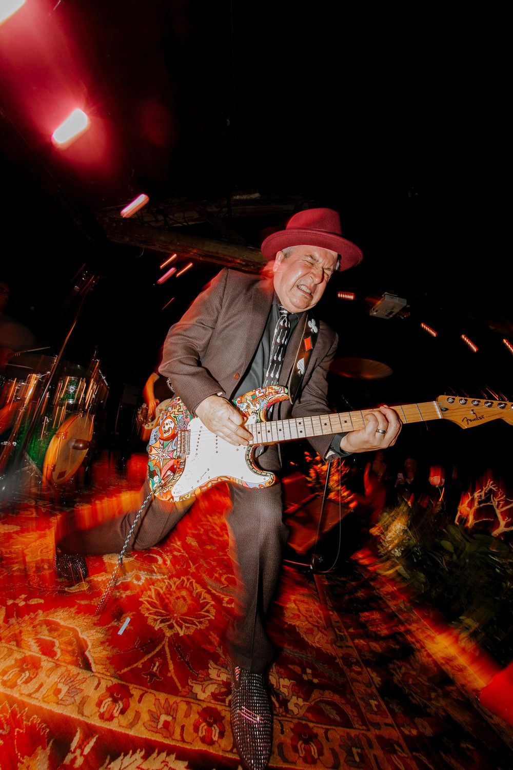 Energetic guitarist in red hat performing on stage with decorative Stratocaster guitar.