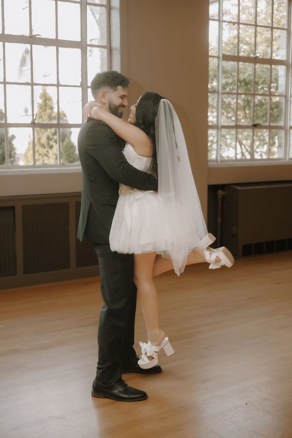 A couple dances intimately in a sunlit room with wooden floors and large windows.