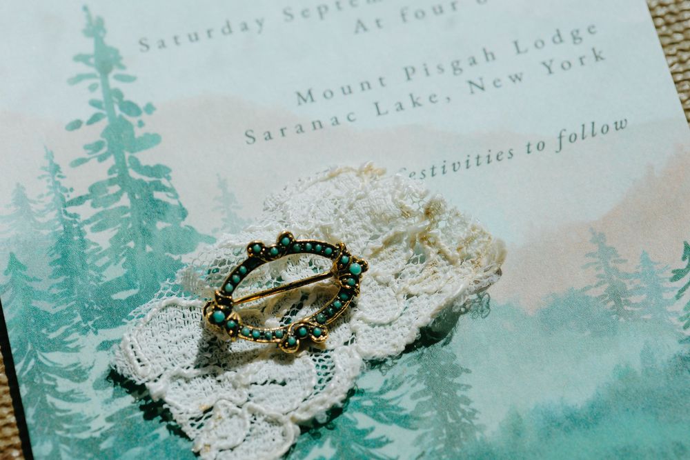 Vintage wedding invitation details with watercolor pine trees and elegant calligraphy text on textured paper.
