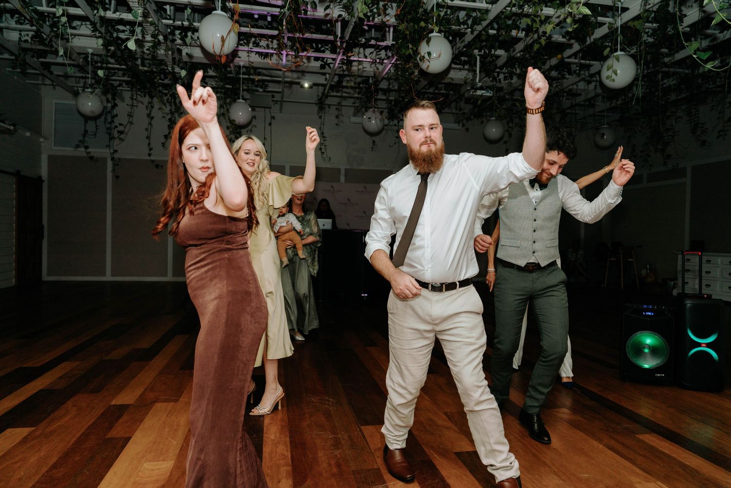 Wedding guests dance and celebrate together on a dimly lit dance floor decorated with hanging lanterns.