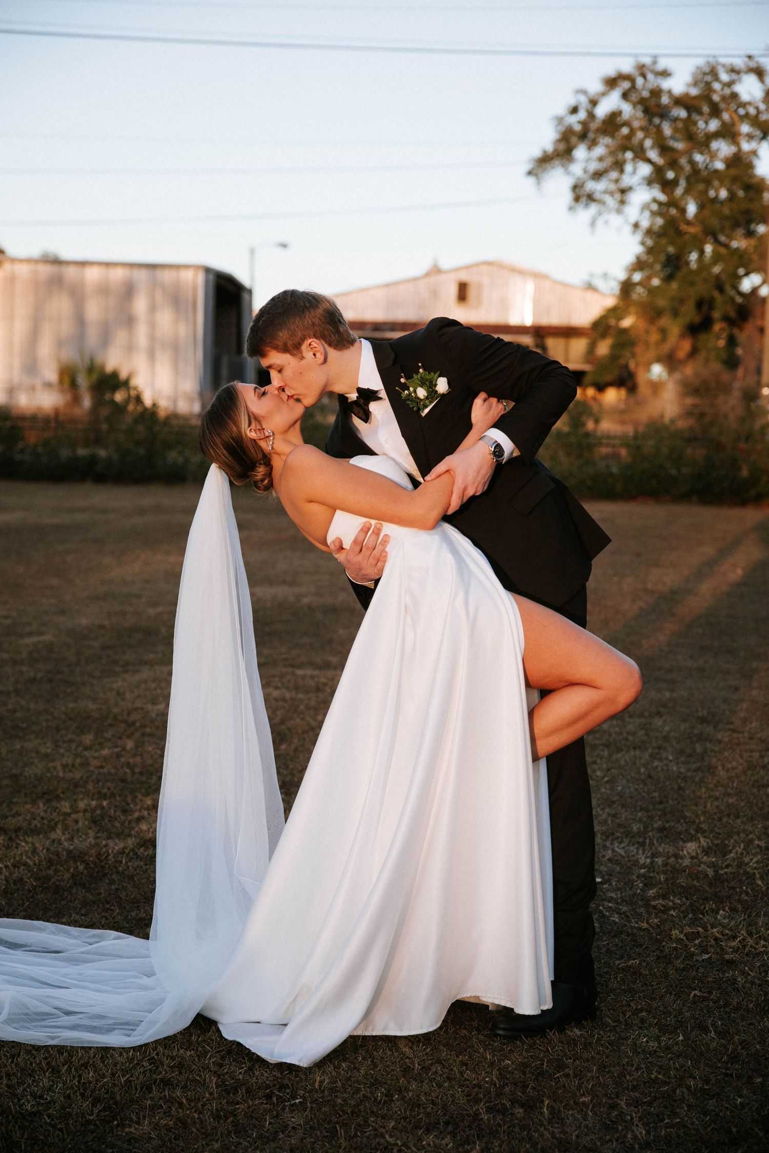 Artistic wedding poses in an open field with dramatic white dress movement at sunset.