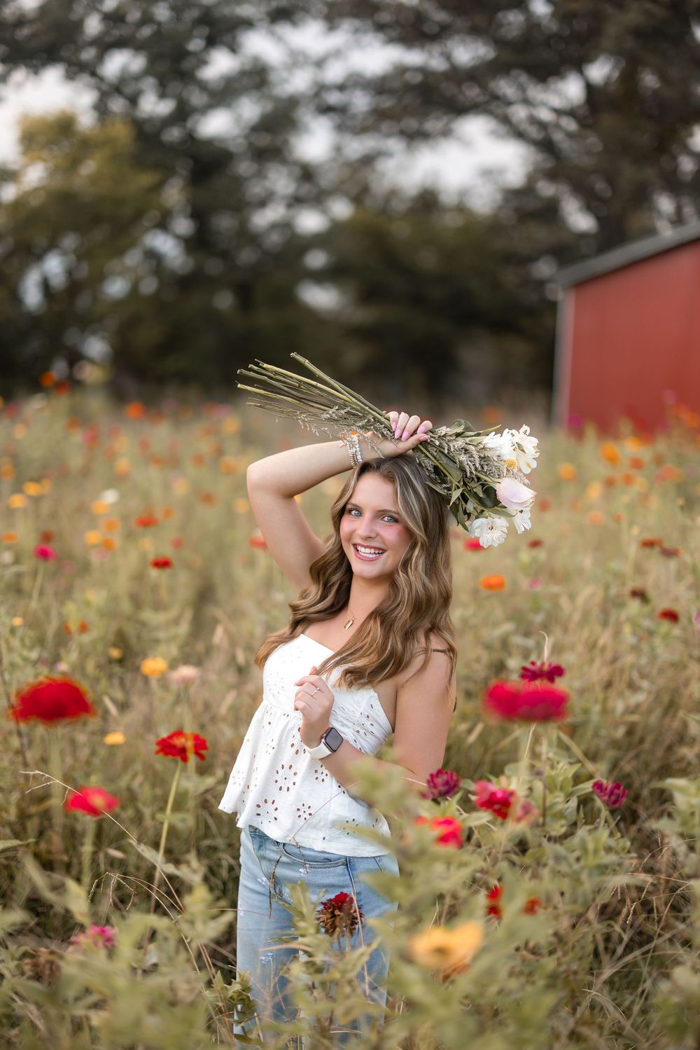 A person in a white lace top and jeans stands in a vibrant wildflower field with red poppies and yellow blooms.