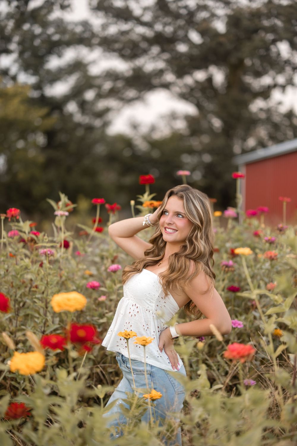 Person in white top posing in a vibrant wildflower field filled with red and yellow blooms on a sunny day.