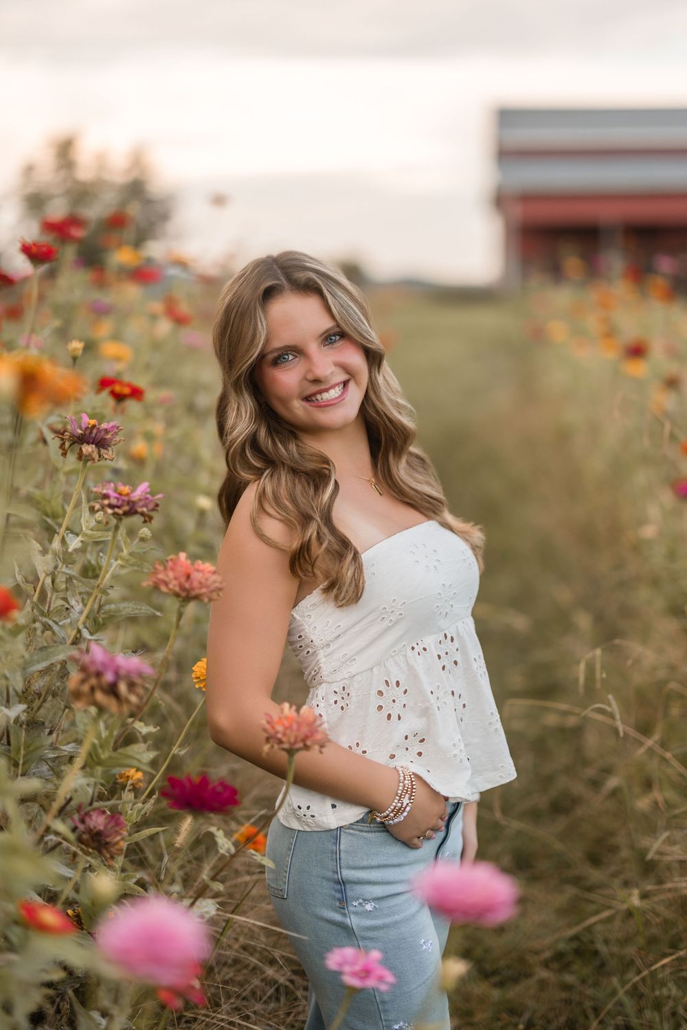 A young person poses among colorful wildflowers in a field at sunset wearing a white eyelet top and denim.