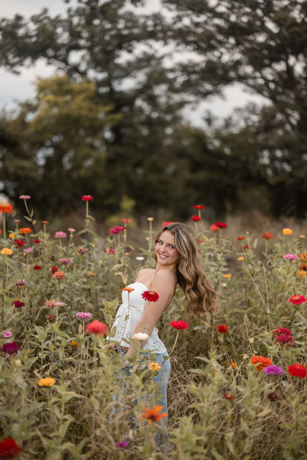 A woman in a white top poses joyfully in a colorful wildflower field during golden hour.