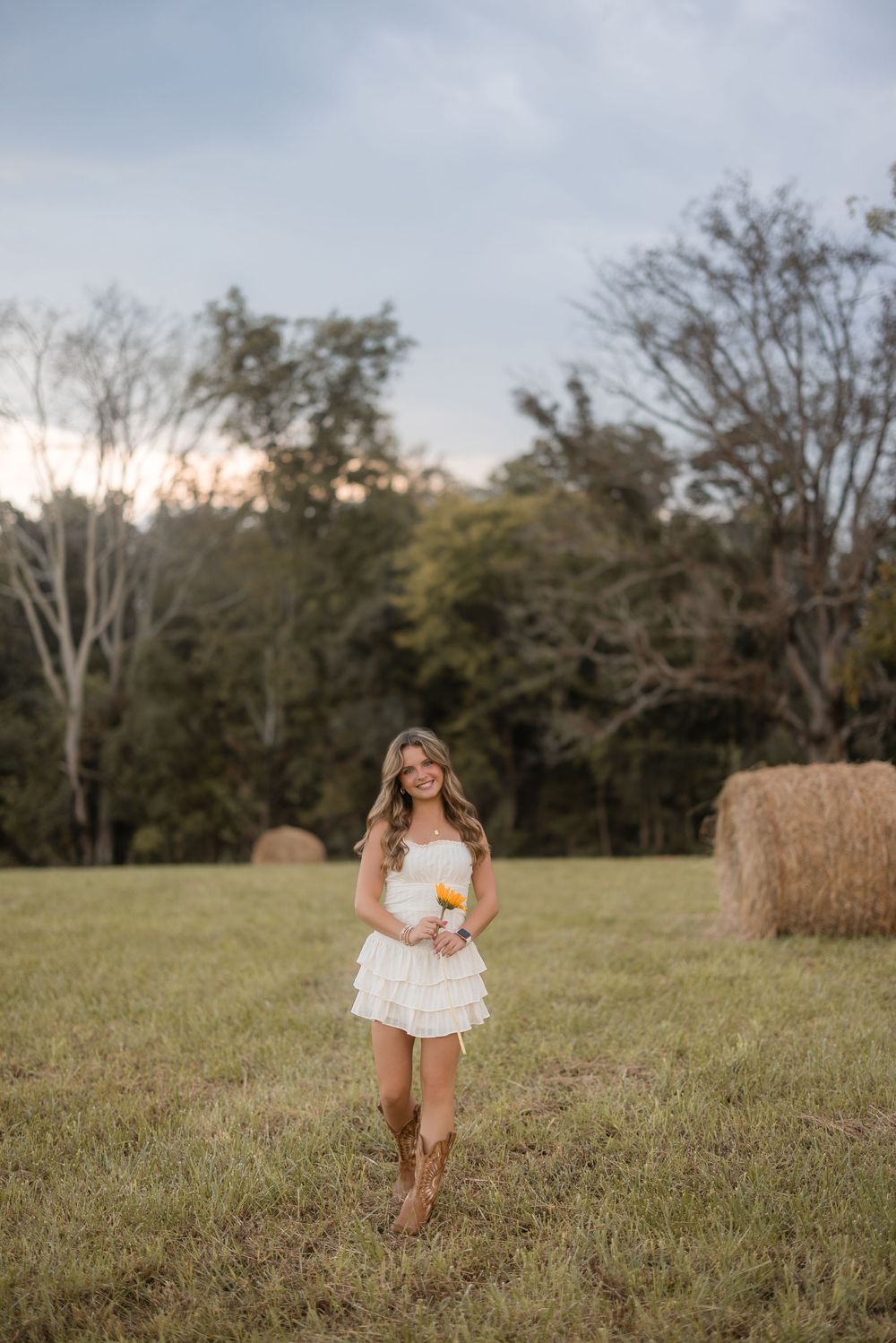 A candid outdoor portrait session in a grassy field with natural light and rustic hay bales in the background.