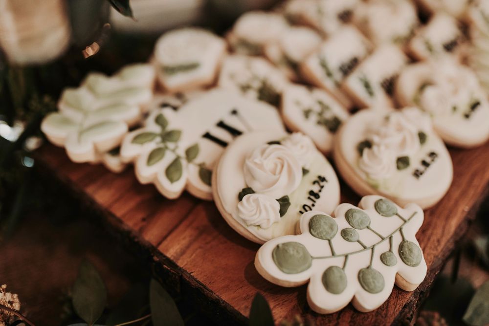 Greenery garlands draped across farmhouse tables surround gourmet wedding cookies at Whispering Oaks Wedding Venue