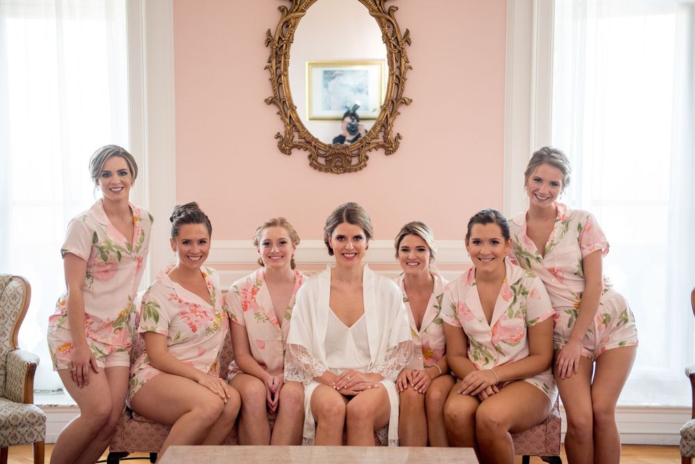 Group in matching pink robes posed together in an elegant room with ornate mirror.