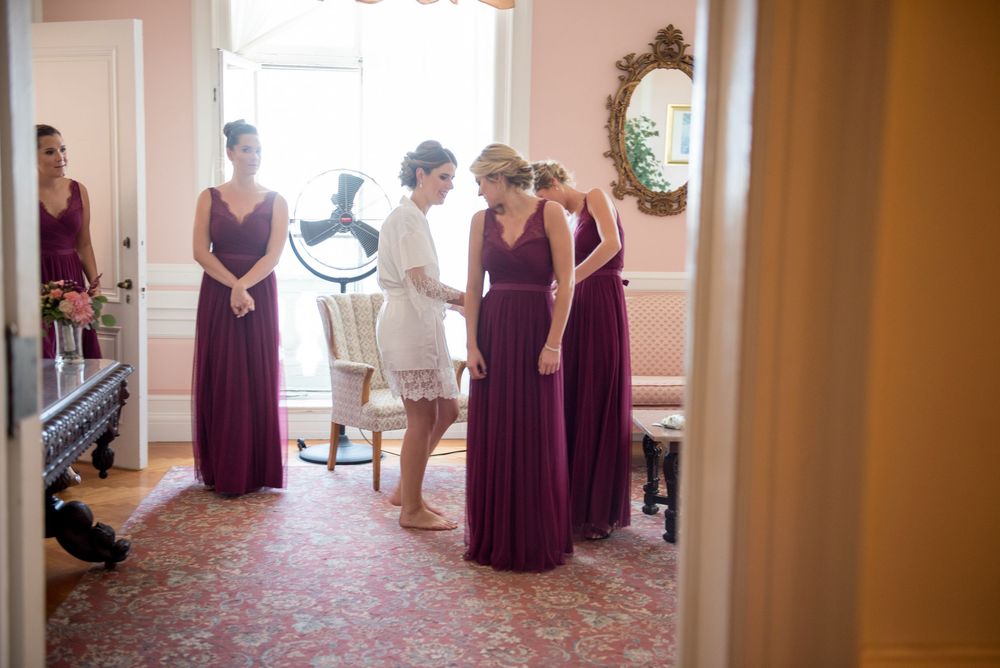 Wedding preparation scene in pink room with purple dresses and white gown.