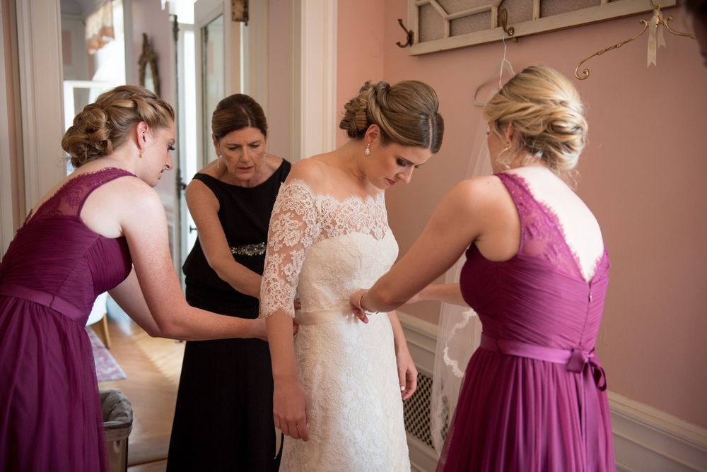 Wedding party helping with dress preparations in a room with pink walls and classic decor.