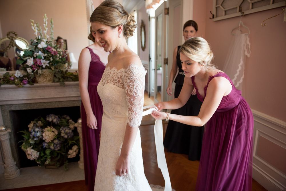 Bridal party assisting with wedding dress details in an elegant room.