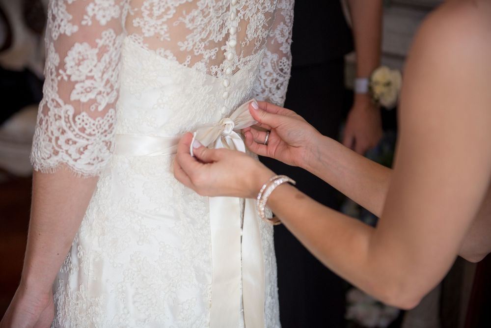 Close-up details of white lace wedding dress being adjusted.