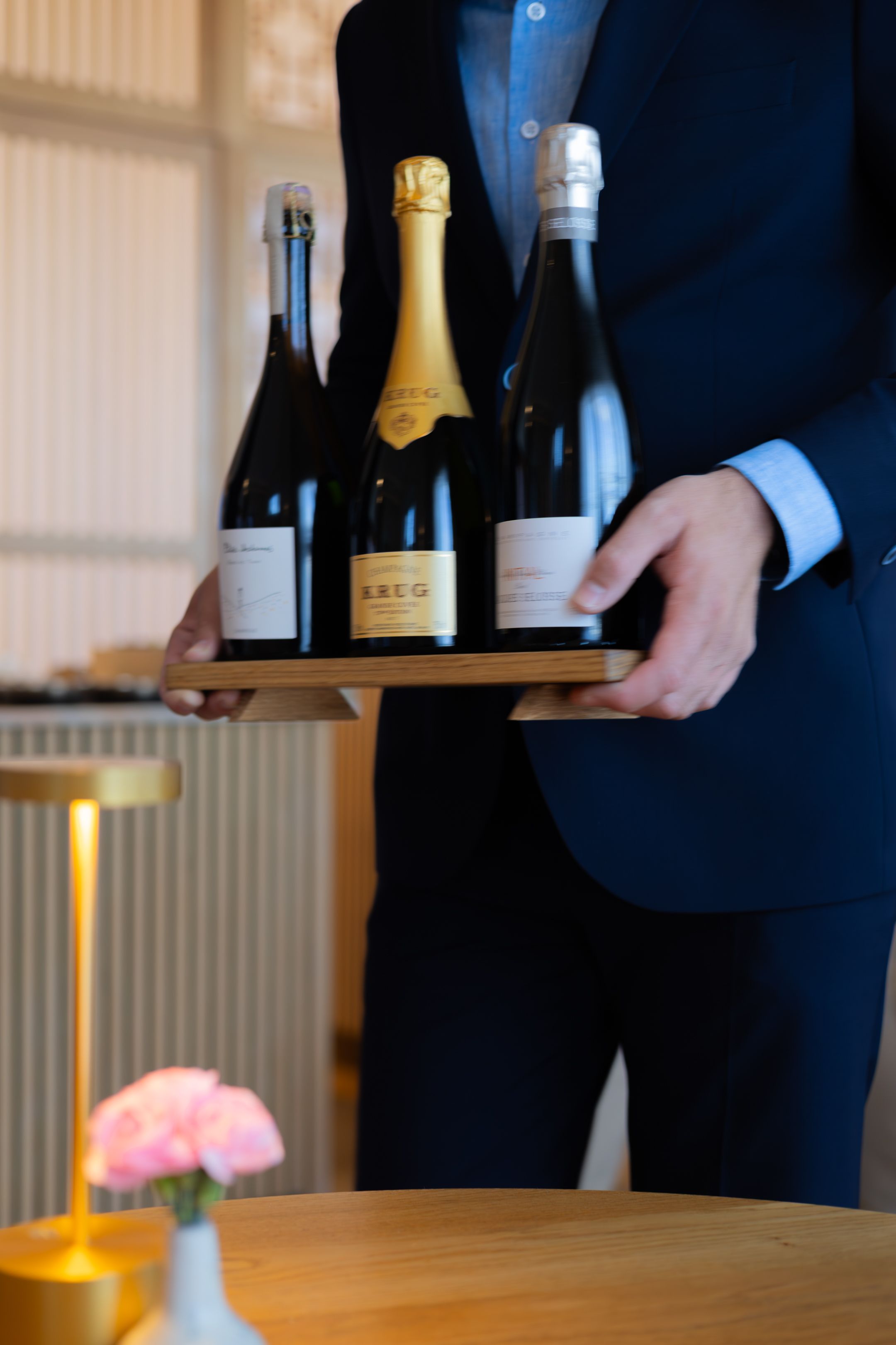Close up view of someone in formal attire holding multiple wine bottles during service or presentation.