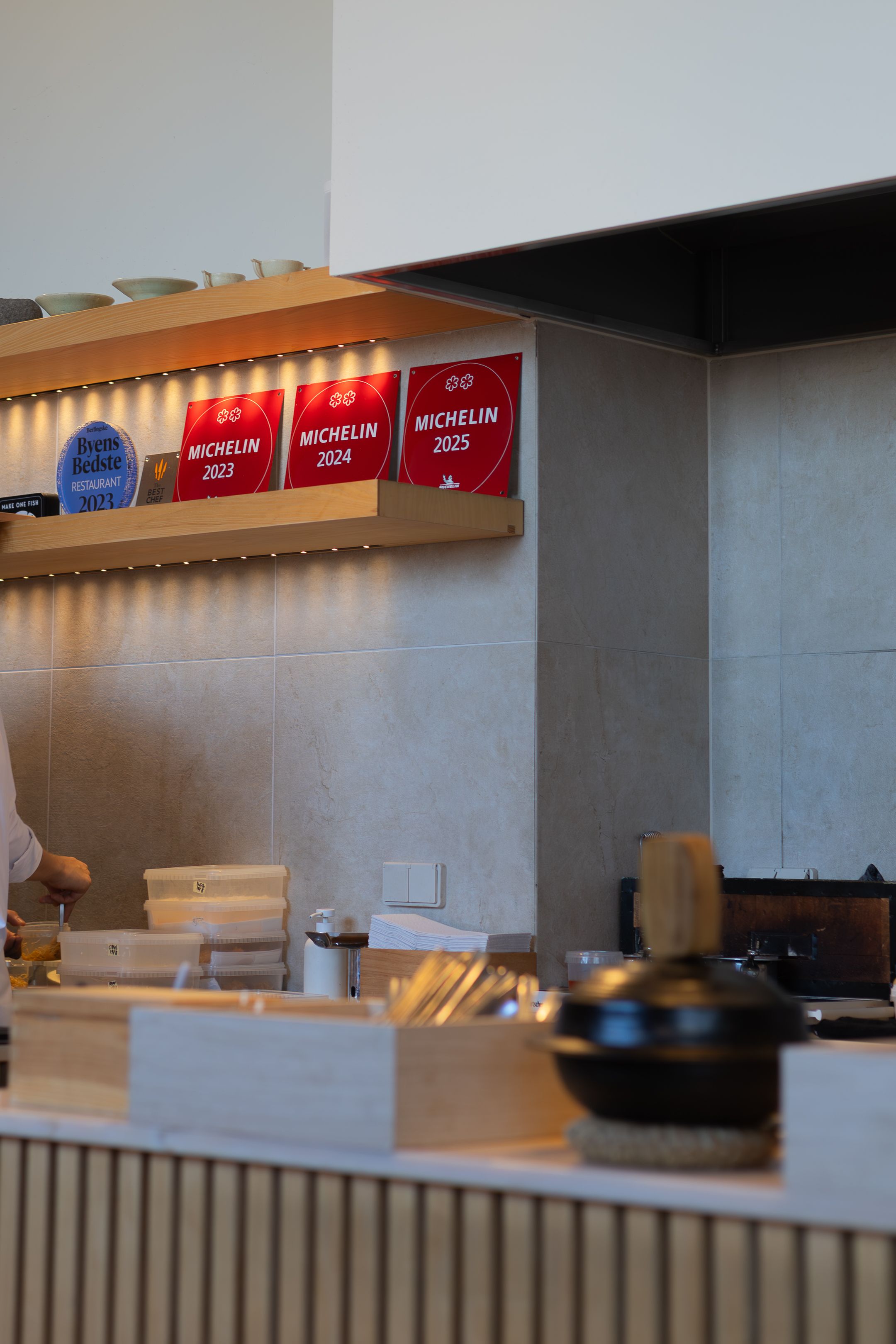 Interior view of a modern restaurant kitchen counter with Michelin star plaques displayed on the wall.