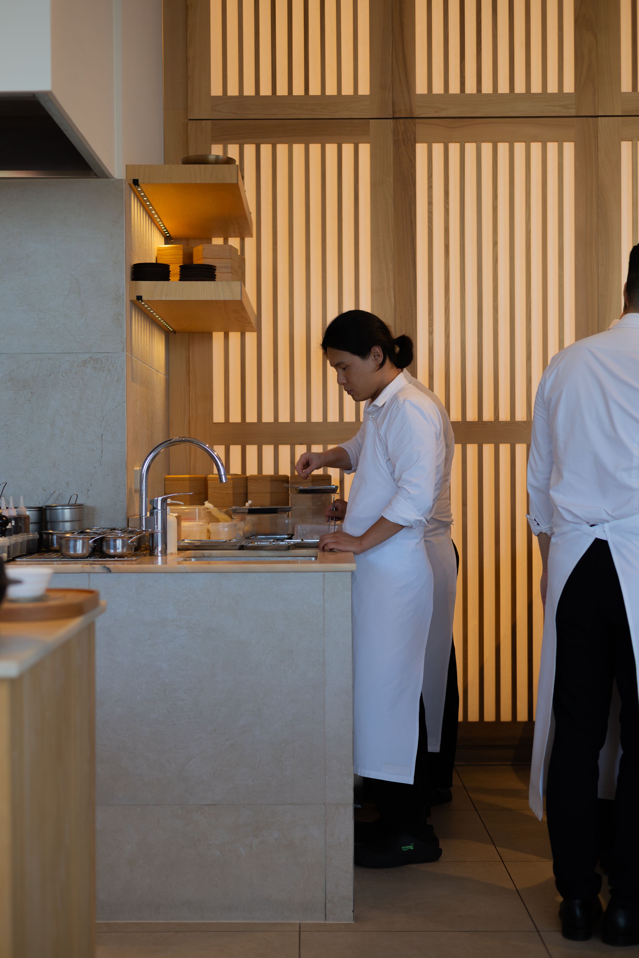 Restaurant kitchen staff preparing meals behind a sleek modern counter with Japanese-inspired wooden screens.