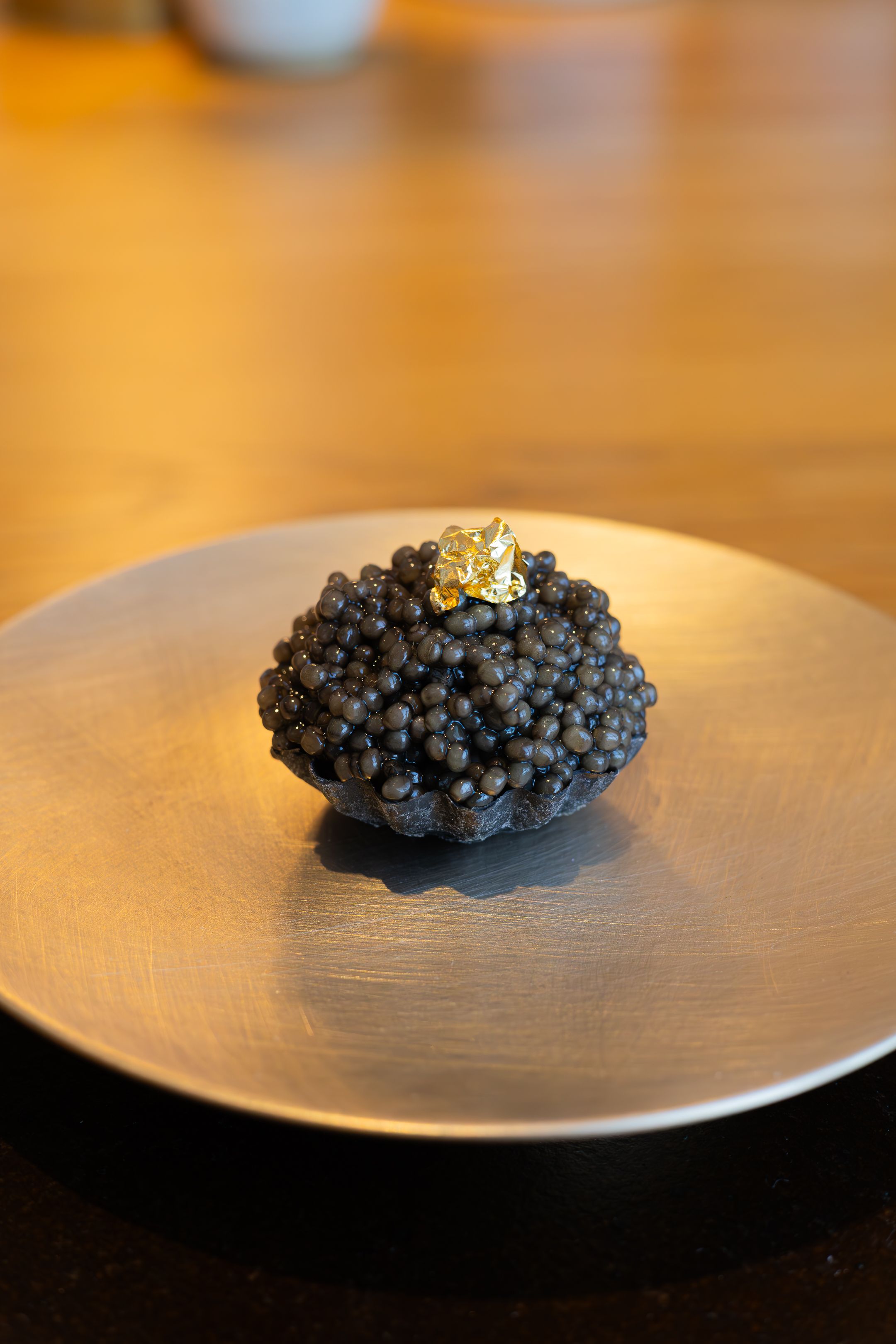 Black caviar served on a round porcelain plate set against a warm wood background with rich amber lighting.