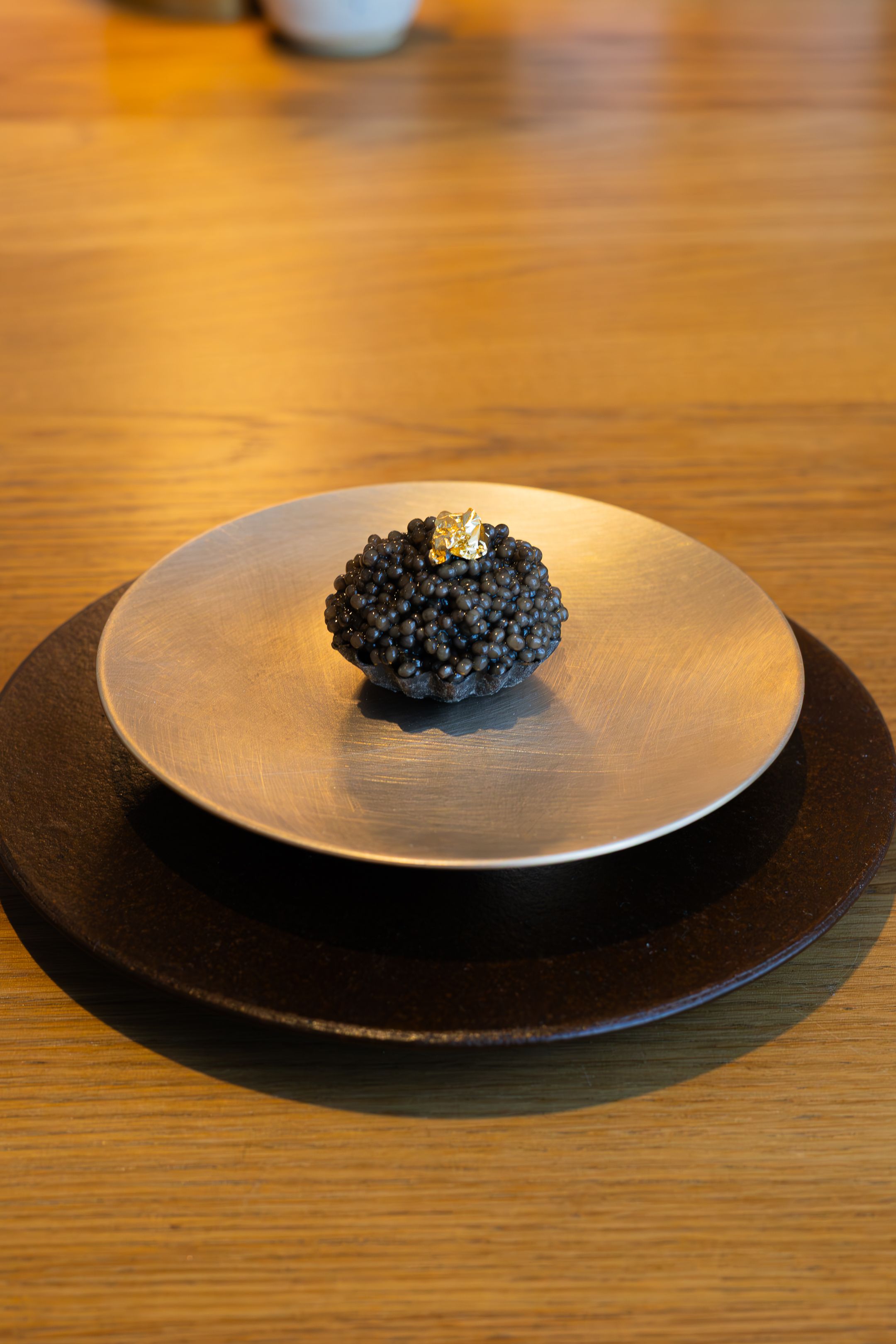 A plate of black caviar presented elegantly in a minimalist style on a white ceramic dish against a wooden table surface.