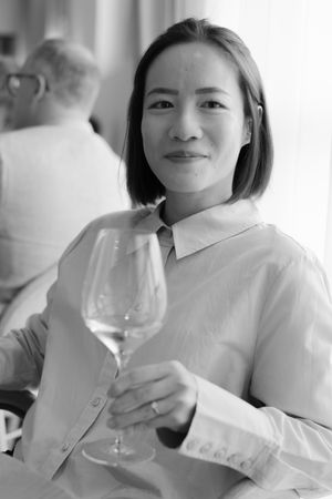 A person in a white button-up shirt holding a wine glass while sitting in a restaurant, captured in black and white.