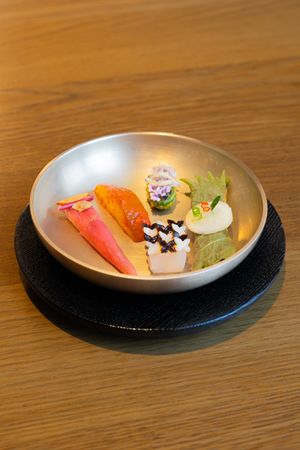 An artistic plating of colorful sashimi and garnishes served in a modern gray ceramic bowl on a wooden table.