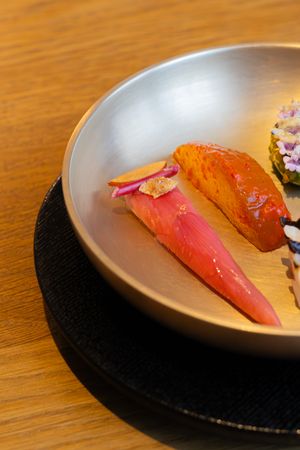 A close-up view of sashimi pieces arranged on a gray plate against a wooden table surface.