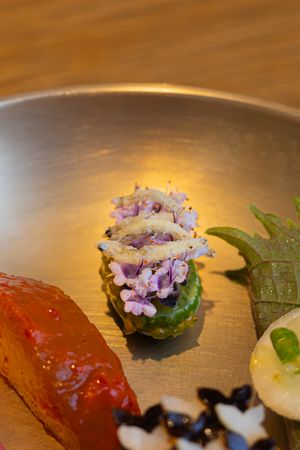 Elegant plated dish featuring purple flowers and red meat garnished with green leaves.