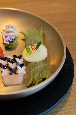 An elegant Japanese appetizer plate featuring delicate sushi pieces and garnishes served in a modern gray bowl.