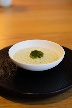 A creamy soup with a green garnish served in a white bowl on a dark plate against a wooden table surface.