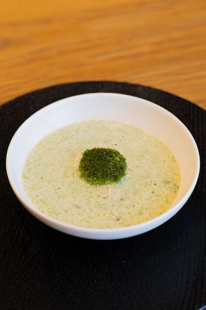 Close-up view of a cream-colored soup with fresh herbs garnished in the center, served on a black plate.