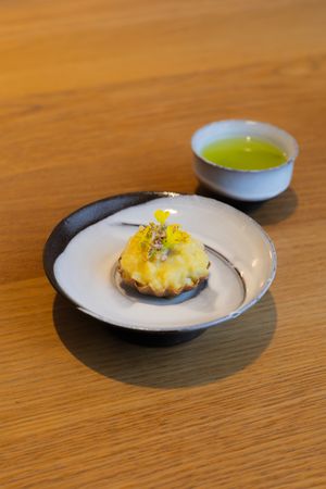 Small plates of elegantly plated yellow garnished bites served on white ceramic dishes against a wooden surface.