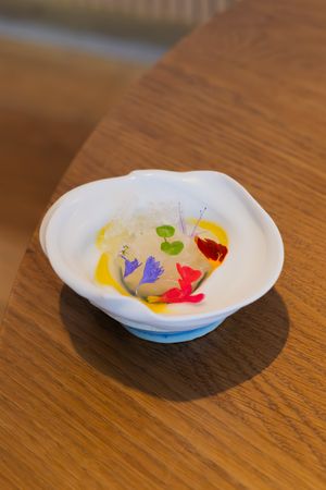 Colorful edible flowers and petals arranged artistically on small white plates against a wooden surface.
