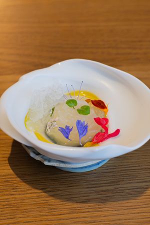 An elegant plated dessert with colorful edible flowers and a creamy center in a white scalloped bowl.
