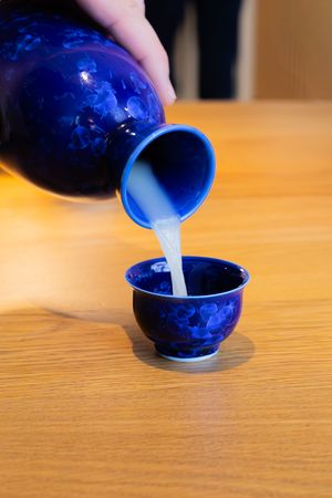 Blue ceramic vessels being filled with white liquid in a sequential pouring demonstration.