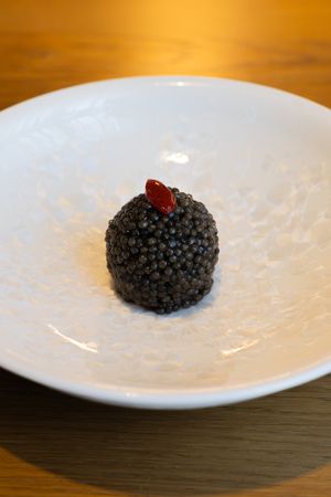 Black caviar served on textured white porcelain plate against dark wood surface.