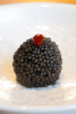 Close-up sequence of black caviar with a single red roe on top served on a white plate.