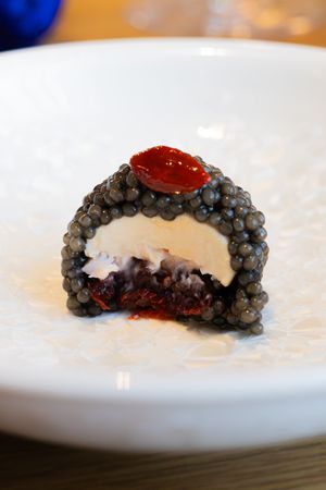 Close-up view of black caviar served on a white plate with red sauce garnish in an upscale dining presentation.