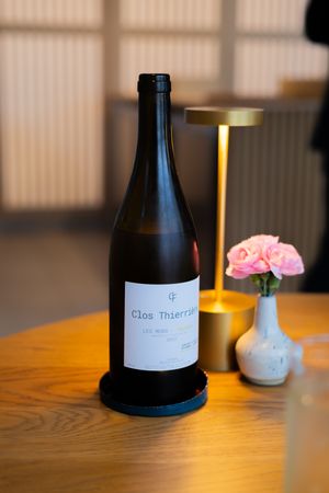 Dark wine bottles with minimalist labels displayed on a wooden table in warm ambient lighting.
