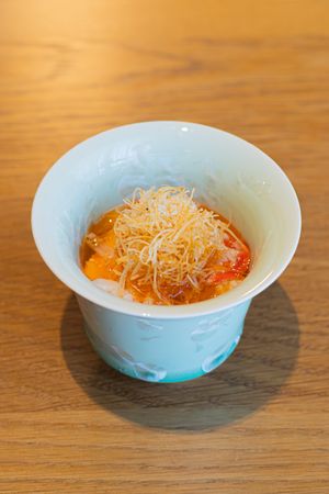 A light blue ceramic bowl containing orange broth garnished with thin crispy noodles.