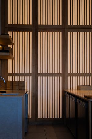 Modern restaurant interior with vertical wooden slats creating a geometric pattern against a dark wall.