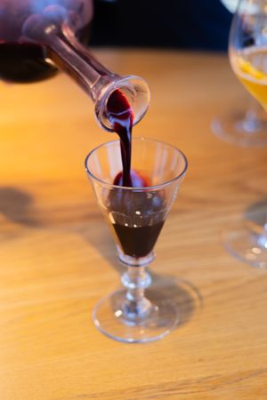 Red wine being poured into crystal stemware on wooden table.