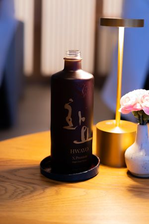 Dark colored glass bottles with decorative labels illuminated by warm lighting on a wooden table.