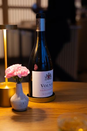Wine bottles and a pink flower arrangement on a wooden table in dim lighting.