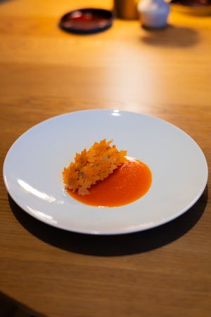 A sequence of white plates showing a diminishing portion of orange-red soup with a crispy garnish on top.