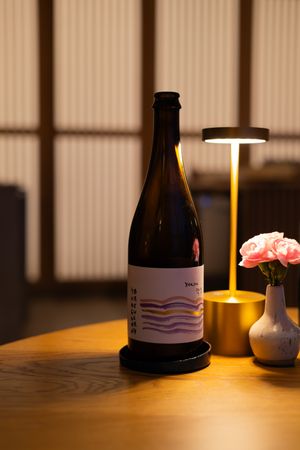 Dark wine bottles and table lamp creating moody ambient lighting on wooden surface.