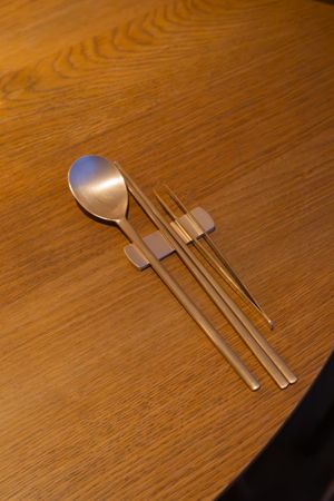 Modern metallic utensils including chopsticks and a spoon arranged on a wooden table.